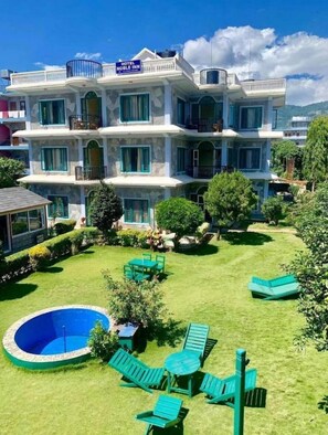 A multi-story hotel with a sign reading "Hotel Noble Inn." It features a well-maintained lawn, a swimming pool, and outdoor seating. - Hotel Noble Inn (Pokhara)