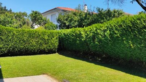 A well-maintained garden with a neatly trimmed hedge, a grassy lawn, and a white building with a red roof in the background. - Relax, silence and sun in the Basque Country (Hendaya)