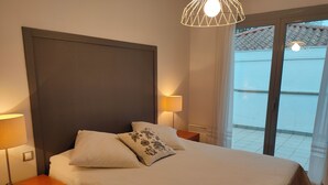 A bedroom with a large bed, two bedside lamps, a wooden nightstand, and a view of the outside through a glass door. - Relax, silence and sun in the Basque Country (Hendaya)