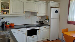 A compact kitchen with white cabinets, a microwave, a refrigerator, and a dining area with a table and chairs. - Relax, silence and sun in the Basque Country (Hendaya)