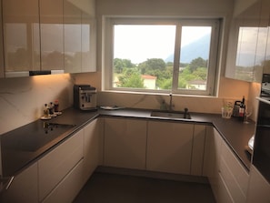 A modern kitchen with a built-in espresso machine, a sink, and a window offering a view of greenery and mountains. - Spacious 3.5-room penthouse in a private location in Ascona (Ascona)