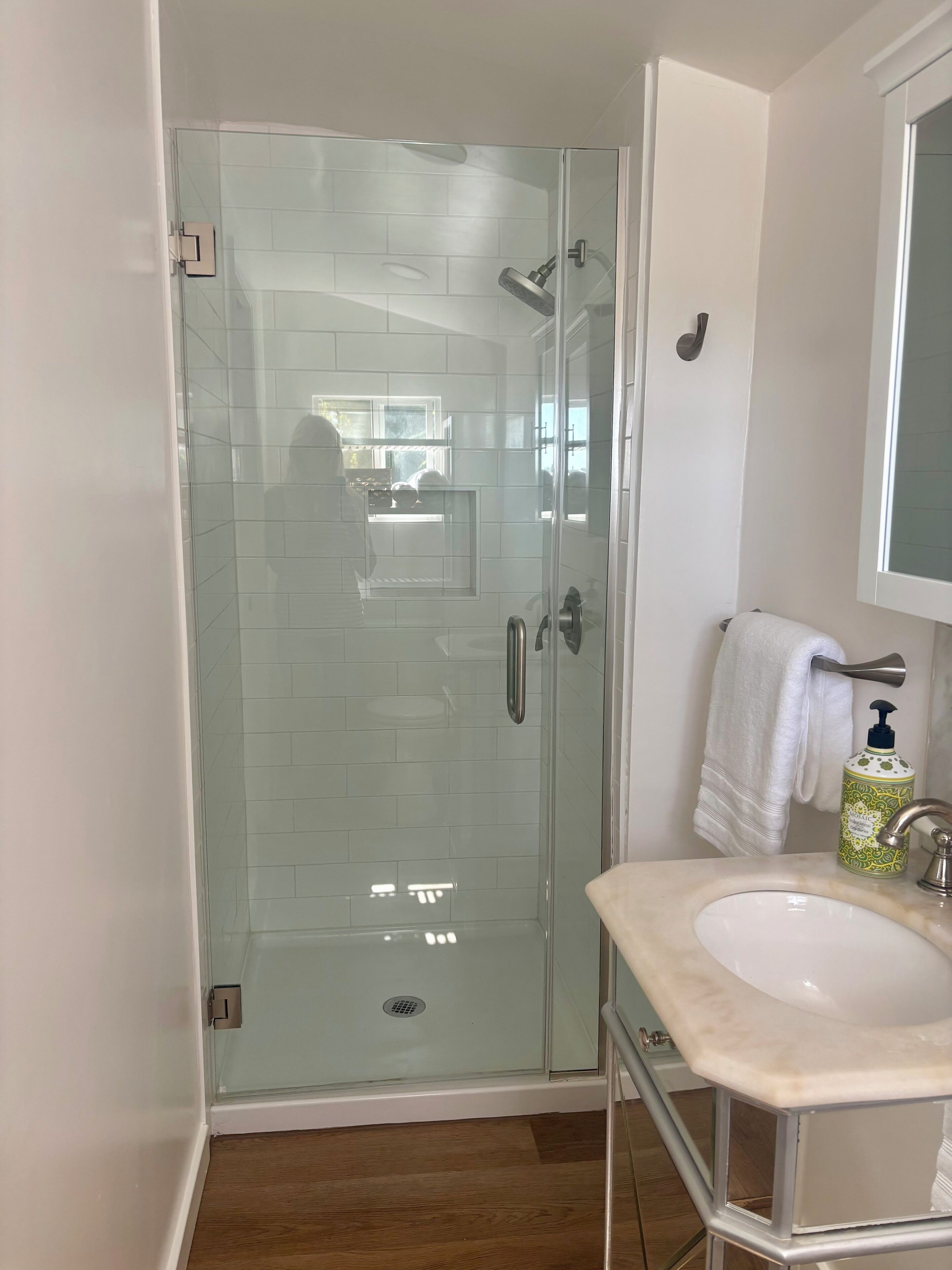 Un baño con ducha de vidrio, lavamanos blanco con encimera de mármol y una toalla colgada en un perchero.