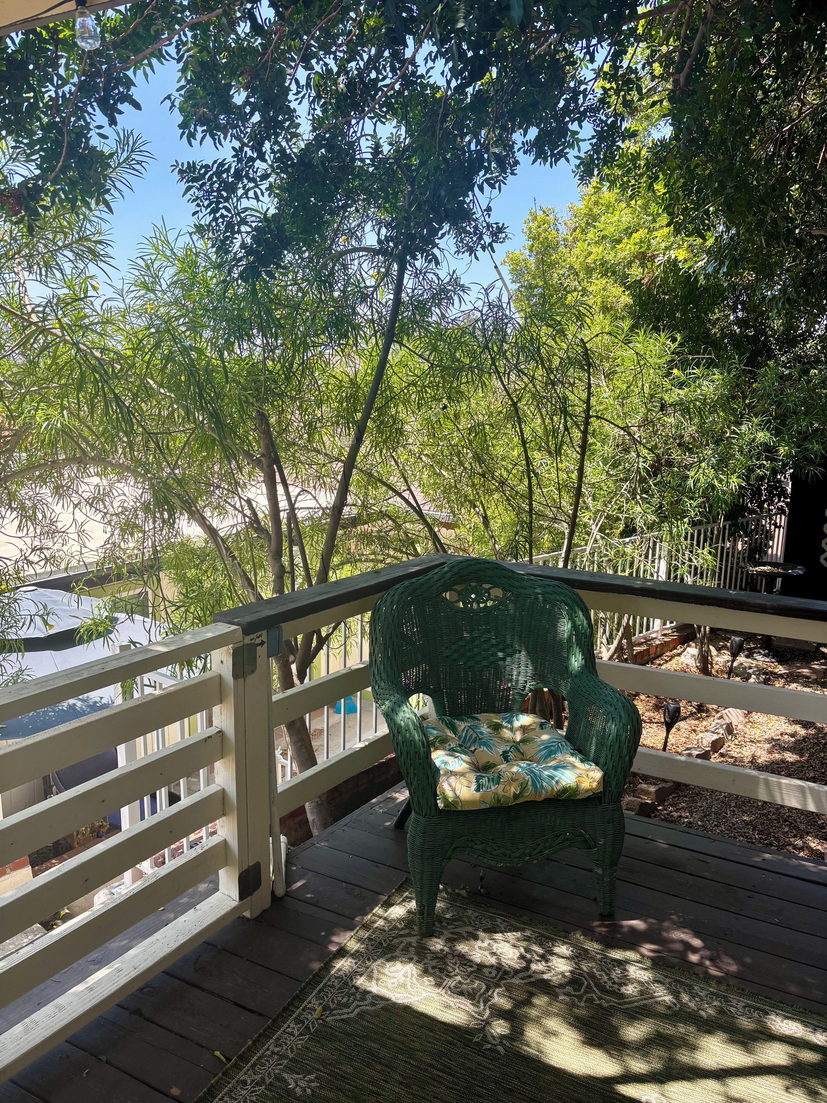 Une terrasse en bois avec une chaise en osier et un tapis à motifs.