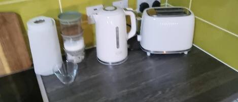 A kitchen counter with a kettle, a toaster, a roll of paper towels, and a glass.