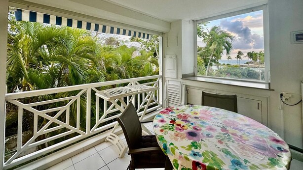 Un balcone con ringhiera bianca, un tavolo con tovaglia a fiori e vista su palme e mare.
