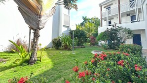 Un giardino curato con diverse piante e fiori, una palma e un edificio bianco con balconi.