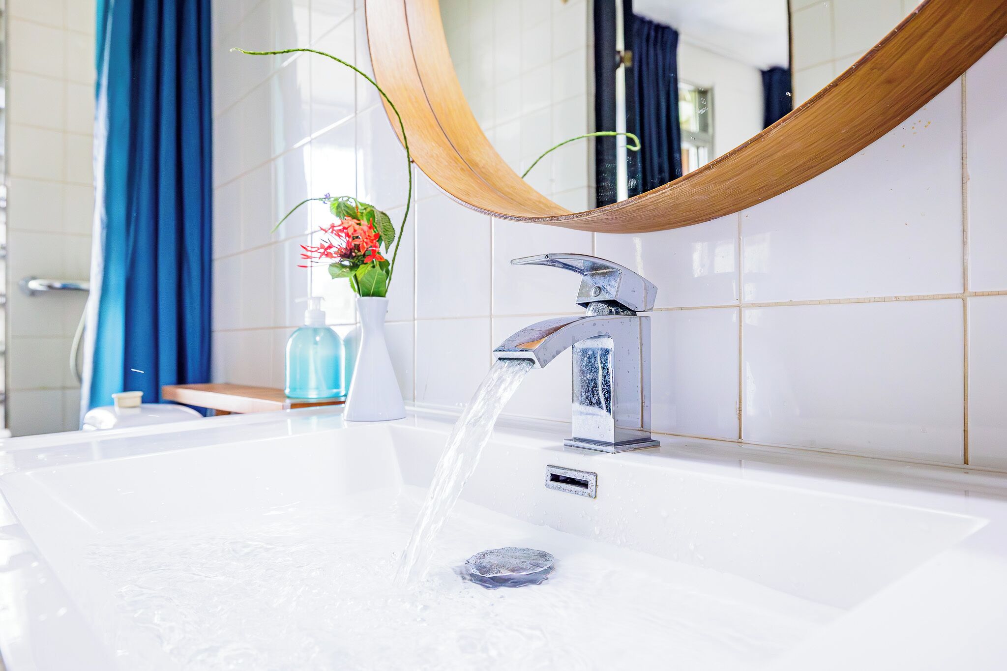 A bathroom with a modern sink, a wooden-framed mirror, and a blue curtain.