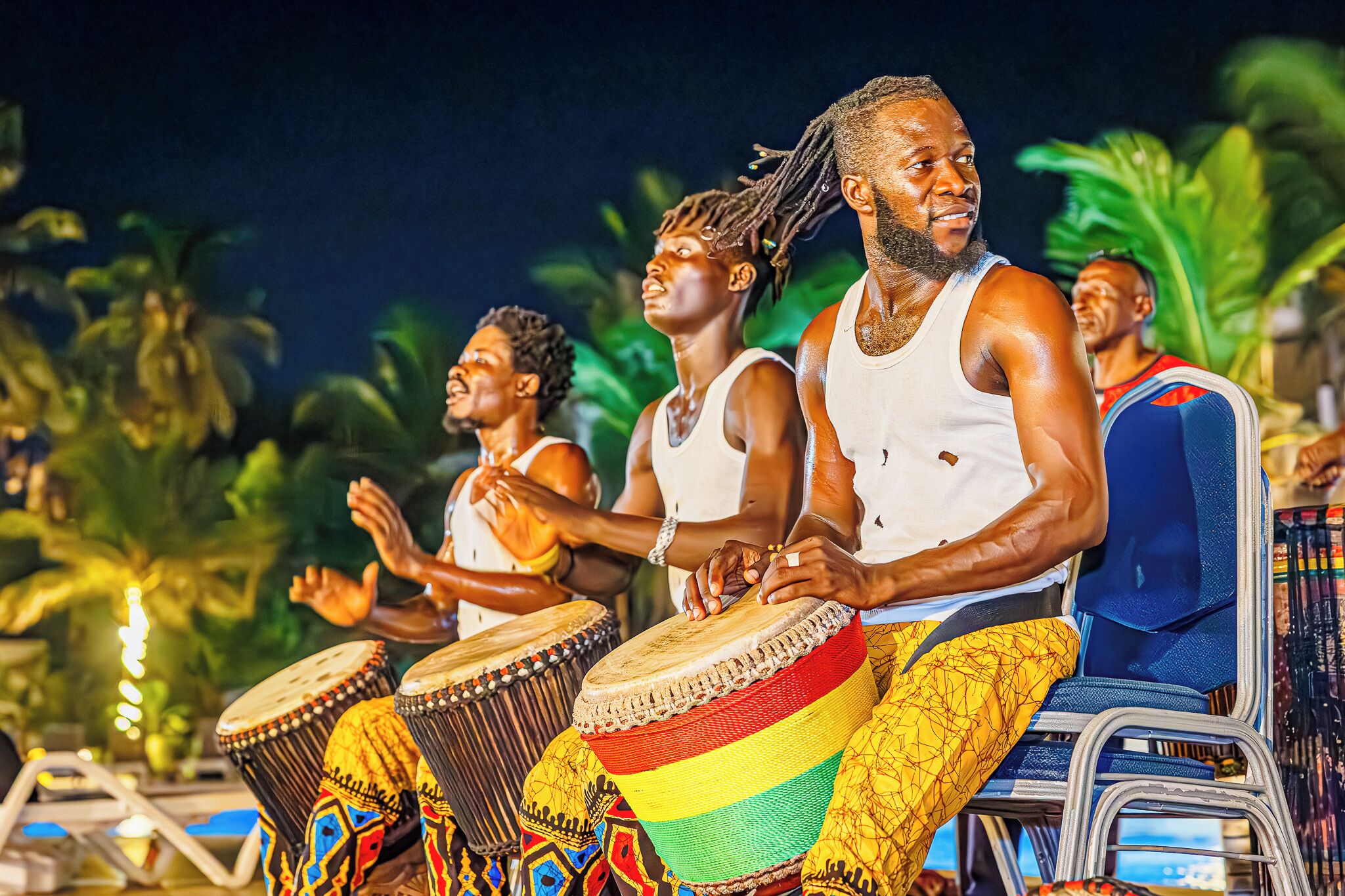 A group of people playing drums in an outdoor setting with palm trees in the background.