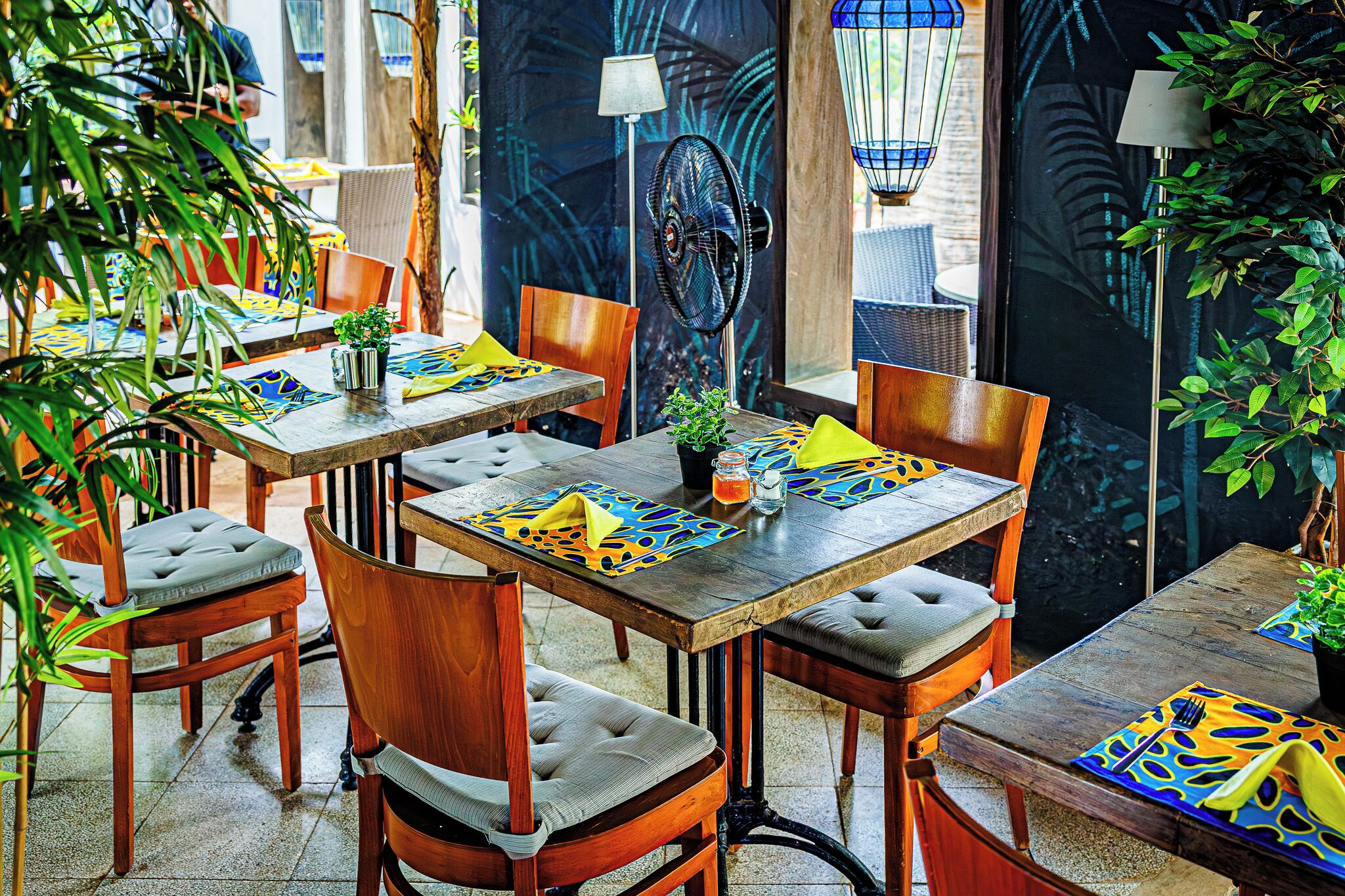 Een restaurant met houten tafels en stoelen, waarvan sommige zijn voorzien van kleurrijke onderzetters.