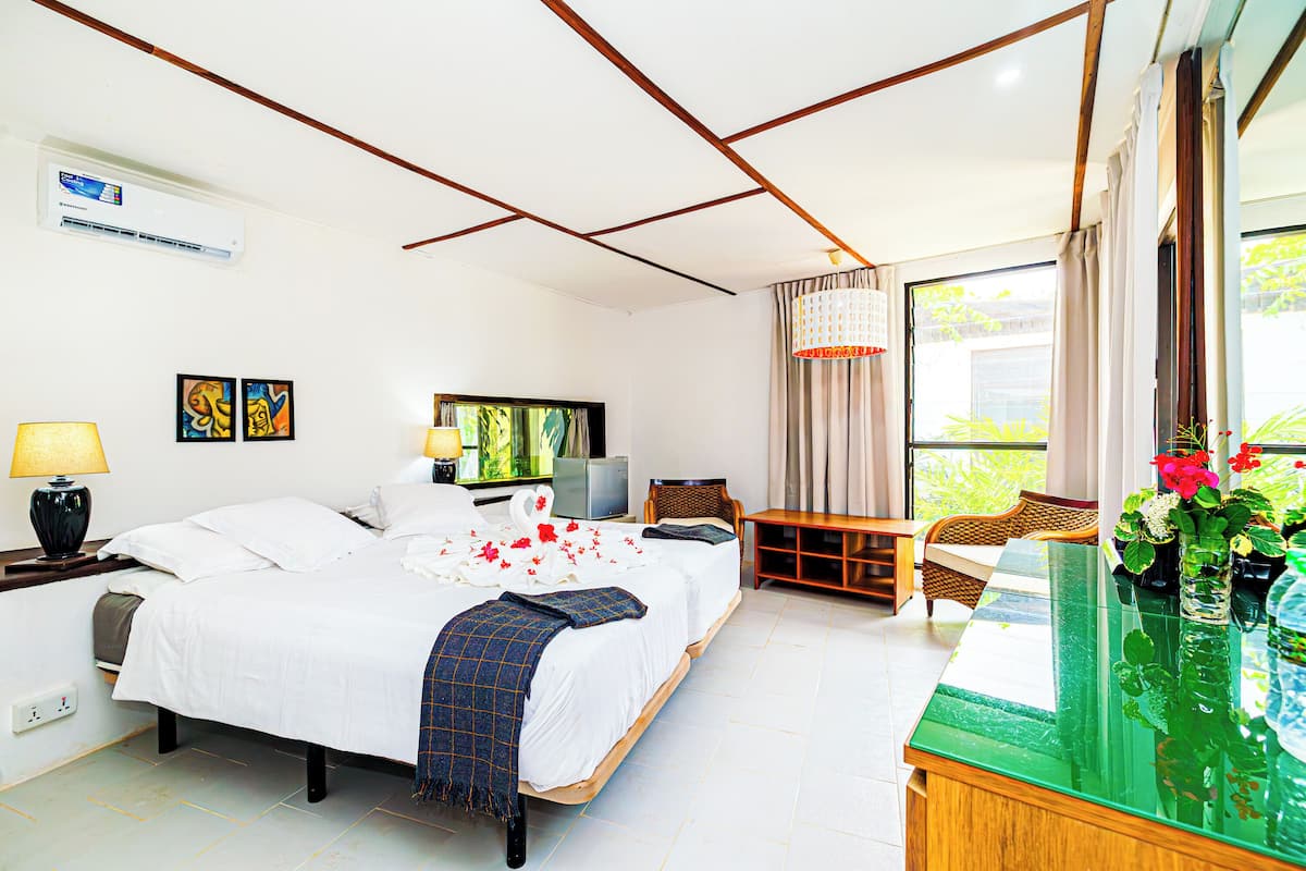 Habitación de hotel con cama, mesitas de noche, escritorio, silla, ventana con cortinas y vistas al exterior.