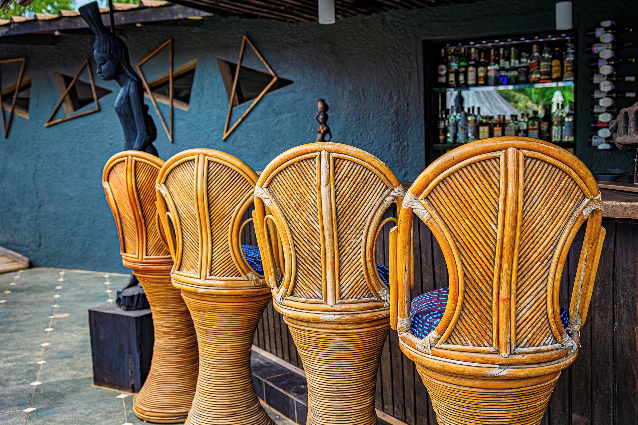 Des chaises en osier avec des coussins bleus, une statue et un coin bar avec des bouteilles.