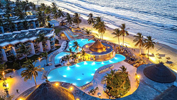 Un resort con una piscina grande, palmeras y acceso a la playa.
