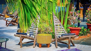 Un espacio al aire libre con ambiente tropical, con sillones de mimbre y un taburete tejido.