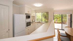 Uma cozinha moderna com armários brancos, forno embutido e uma grande janela com vista para um jardim.