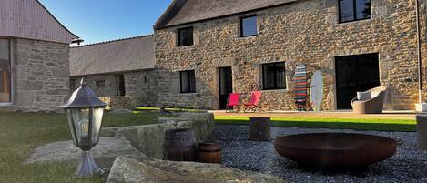 A stone building with a stone roof, a fire pit, and two lounge chairs.