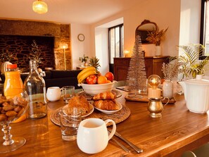 Ein Esstisch mit Früchten, Gebäck und Getränken, platziert in einem gemütlichen Zimmer mit Kamin und Weihnachtsbaum.