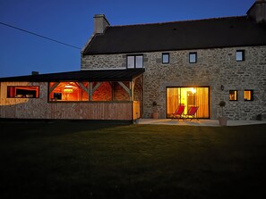 Ein Steinhaus mit einem Holzanbau, ausgestattet mit einer großen Glasdoor und zwei roten Stühlen davor.