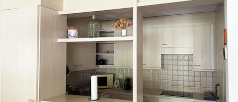 Een compacte keuken met ingebouwde apparaten, waaronder een magnetron, oven en vaatwasser, en een klein aanrecht met een vaas en decoratieve objecten.
