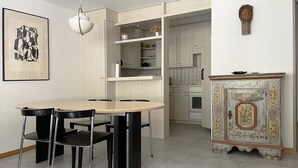 Et spiseområde med et bord og stole, et skab med dekorative detaljer og et køkken i baggrunden.