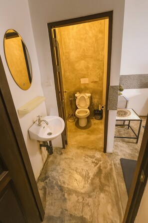 A bathroom with a white sink, a gold-toned toilet, and a small table with a decorative item. - Full Moon Confidence Cave Rest After the Rave (Ko Pha-ngan)