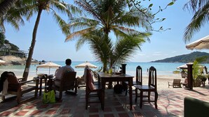 An outdoor seating area with wooden tables and chairs, umbrellas, and a view of the beach and ocean.