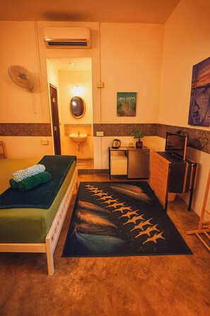 A compact hotel room with a bed, a small desk, a chair, a sink, and an air conditioning unit. - Full Moon Confidence Cave Rest After the Rave (Ko Pha-ngan)