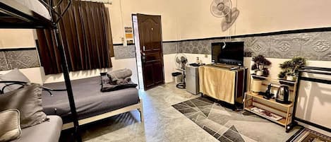 A compact living space with a bunk bed, a sofa, a small kitchenette, and a TV.
