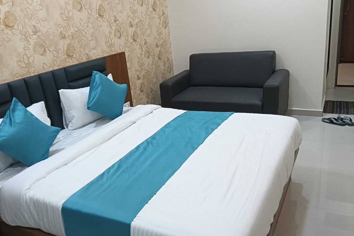 A neatly made bed with a blue and white bedspread, a dark headboard, and two blue pillows. A dark armchair is positioned to the right of the bed.
