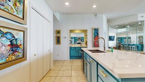 A modern kitchen with teal cabinets, a marble countertop, and a view into the dining area.