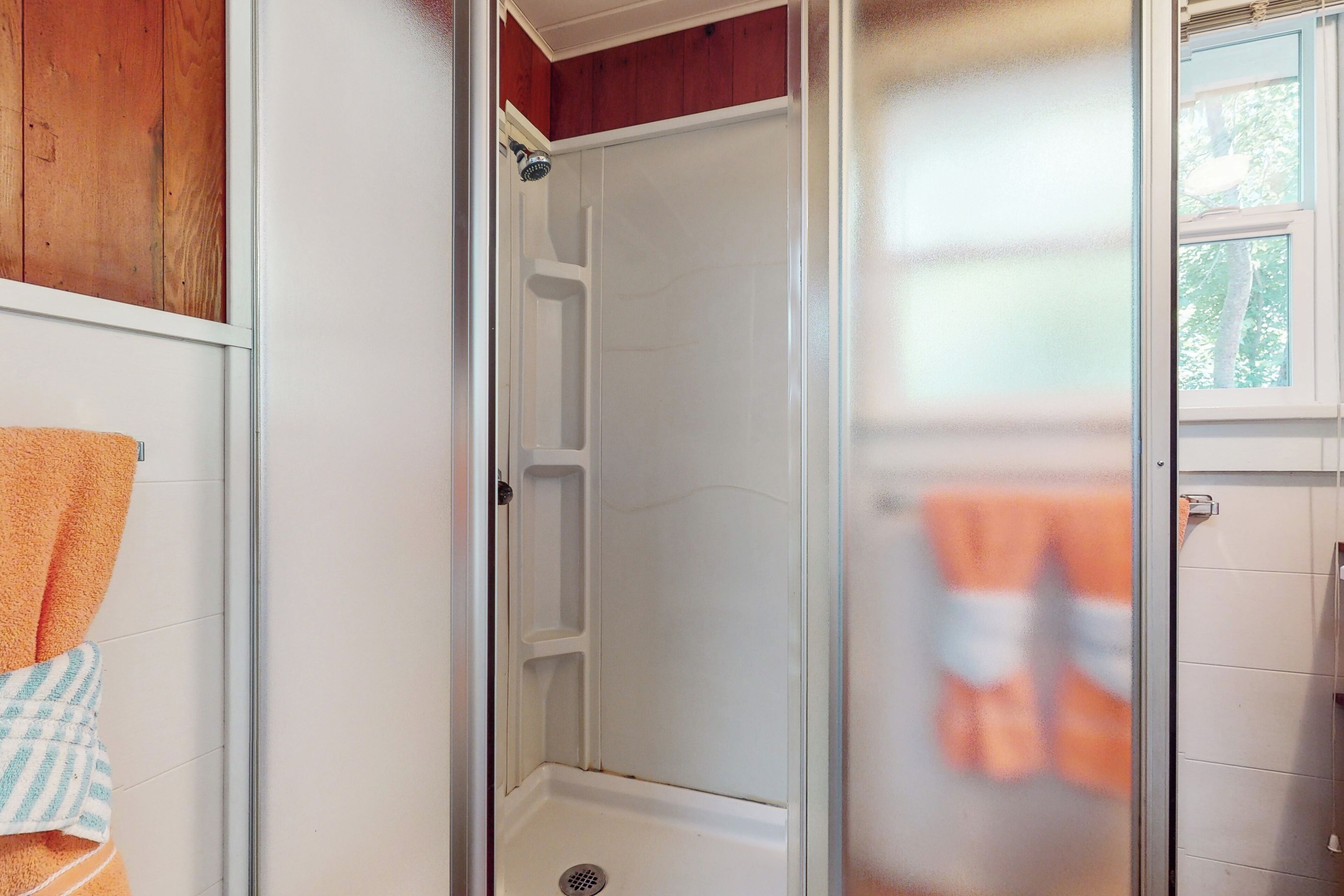 A bathroom with a shower, a towel rack, and a window.