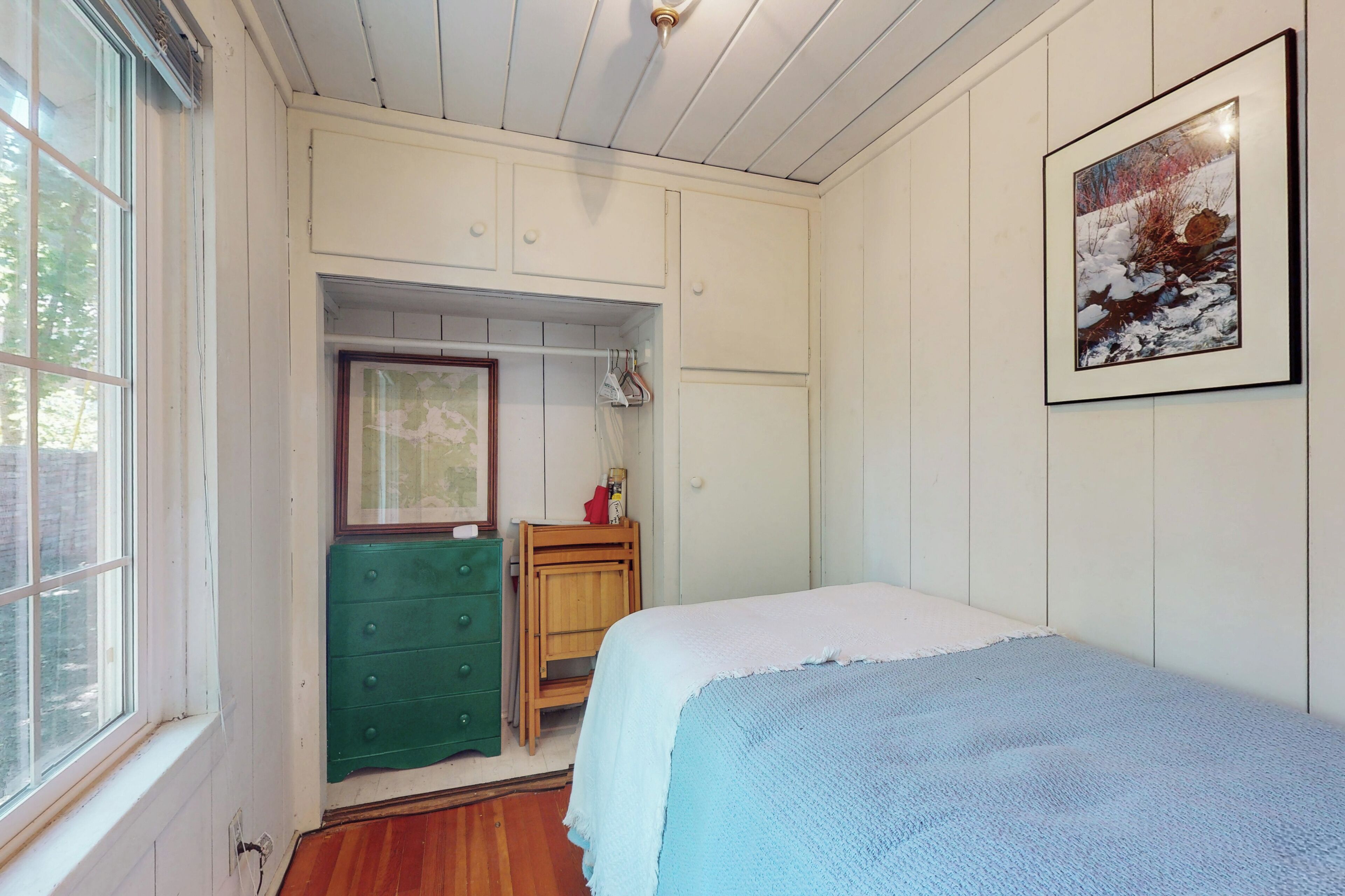 A bedroom with a bed, a green dresser, a wooden cabinet, and a framed picture on the wall.