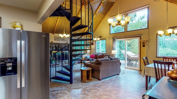 Amplia sala de estar con una escalera espiral, una cocina moderna y grandes ventanales con vistas al exterior.