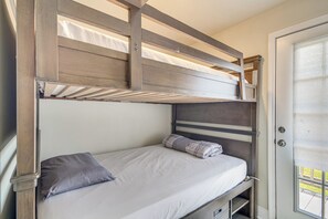 Ein Stockbett mit einer unteren Liege und einer Einzelbett, beide mit Kissen. Eine Tür befindet sich rechts und ein Fenster oben am Stockbett.