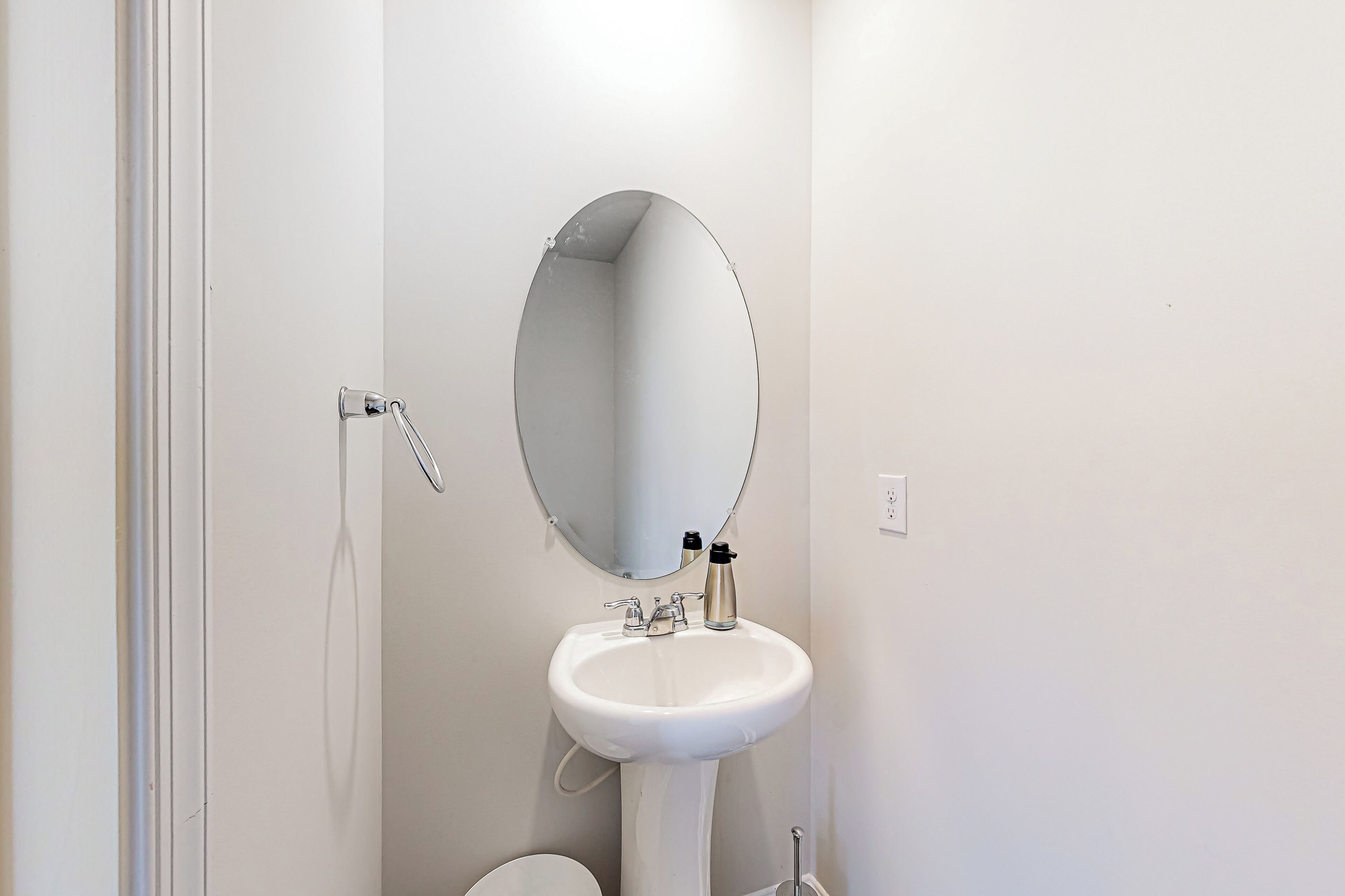 A white bathroom with a round mirror, a white sink, and a toilet.