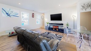 Una sala moderna con un sofá de cuero, una mesa de comedor de vidrio y un televisor de pantalla plana montado en la pared.