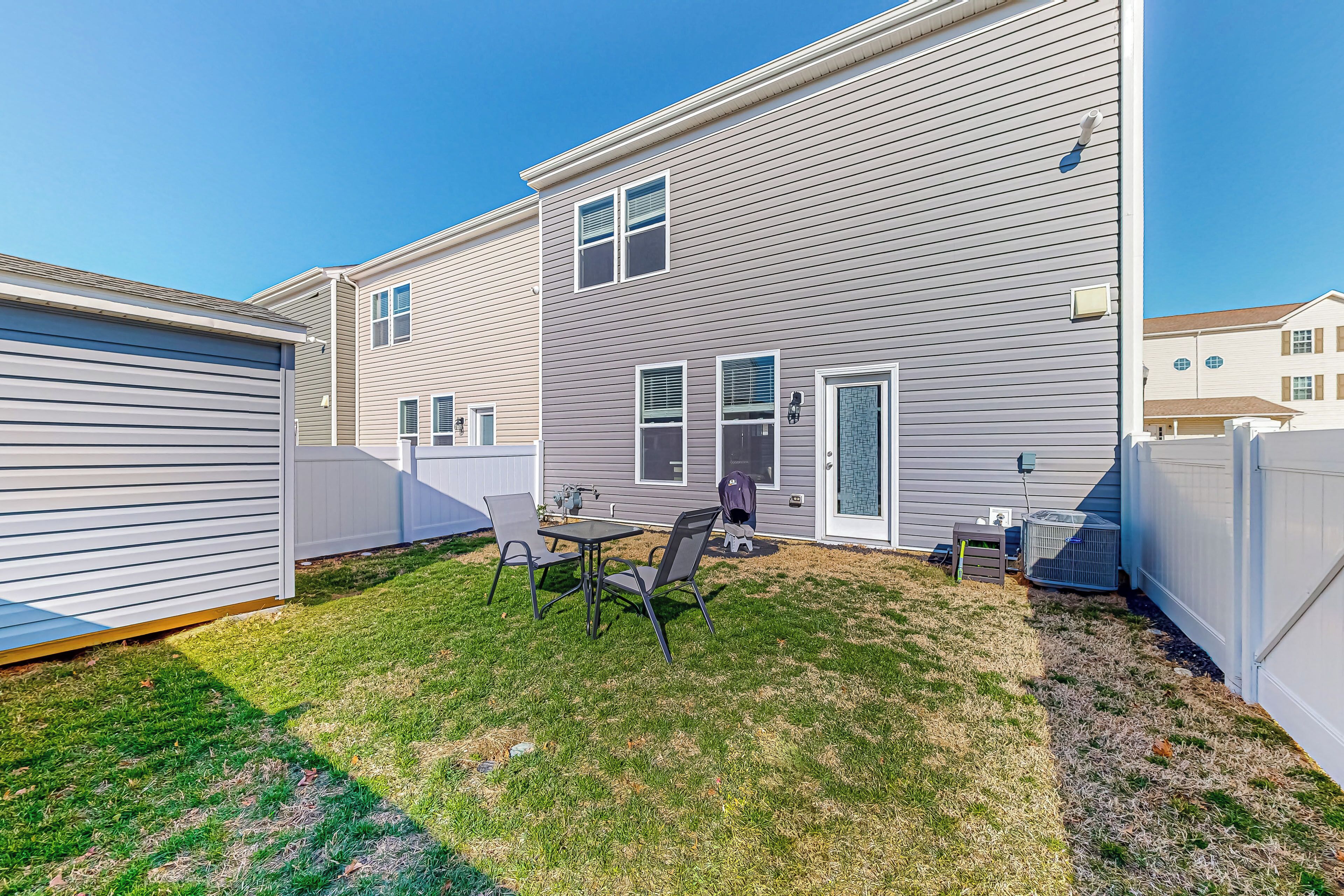 A two-story house with a patio area featuring a table and chairs, a small shed, and an air conditioning unit.