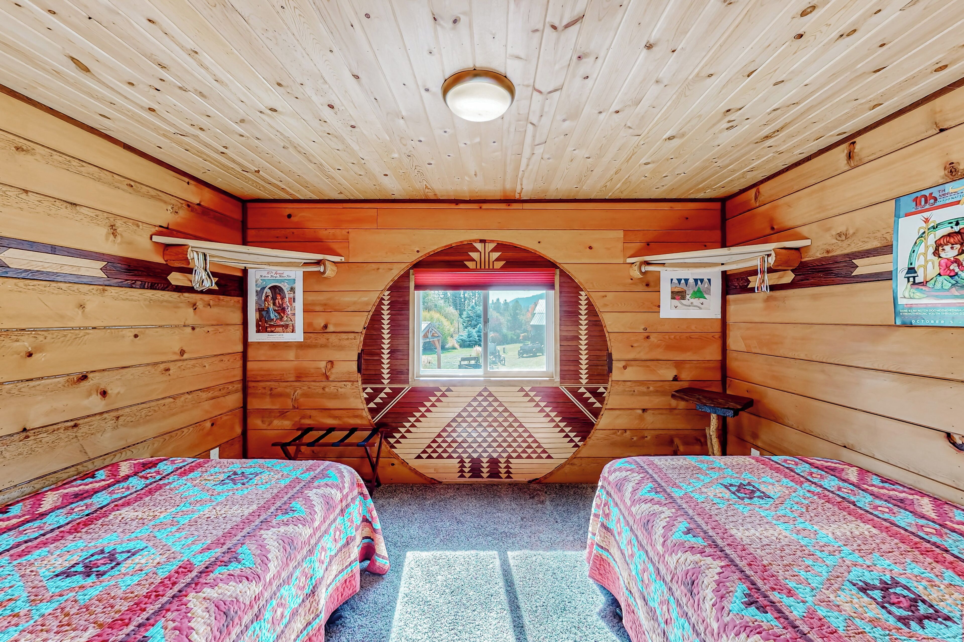 A cozy cabin room with two beds, a window with a decorative arch, and a small table.