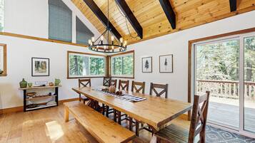 Un vaste espace dédié à la salle à manger, avec une grande table en bois et des bancs, le tout entouré de grandes fenêtres offrant une vue sur l’extérieur.