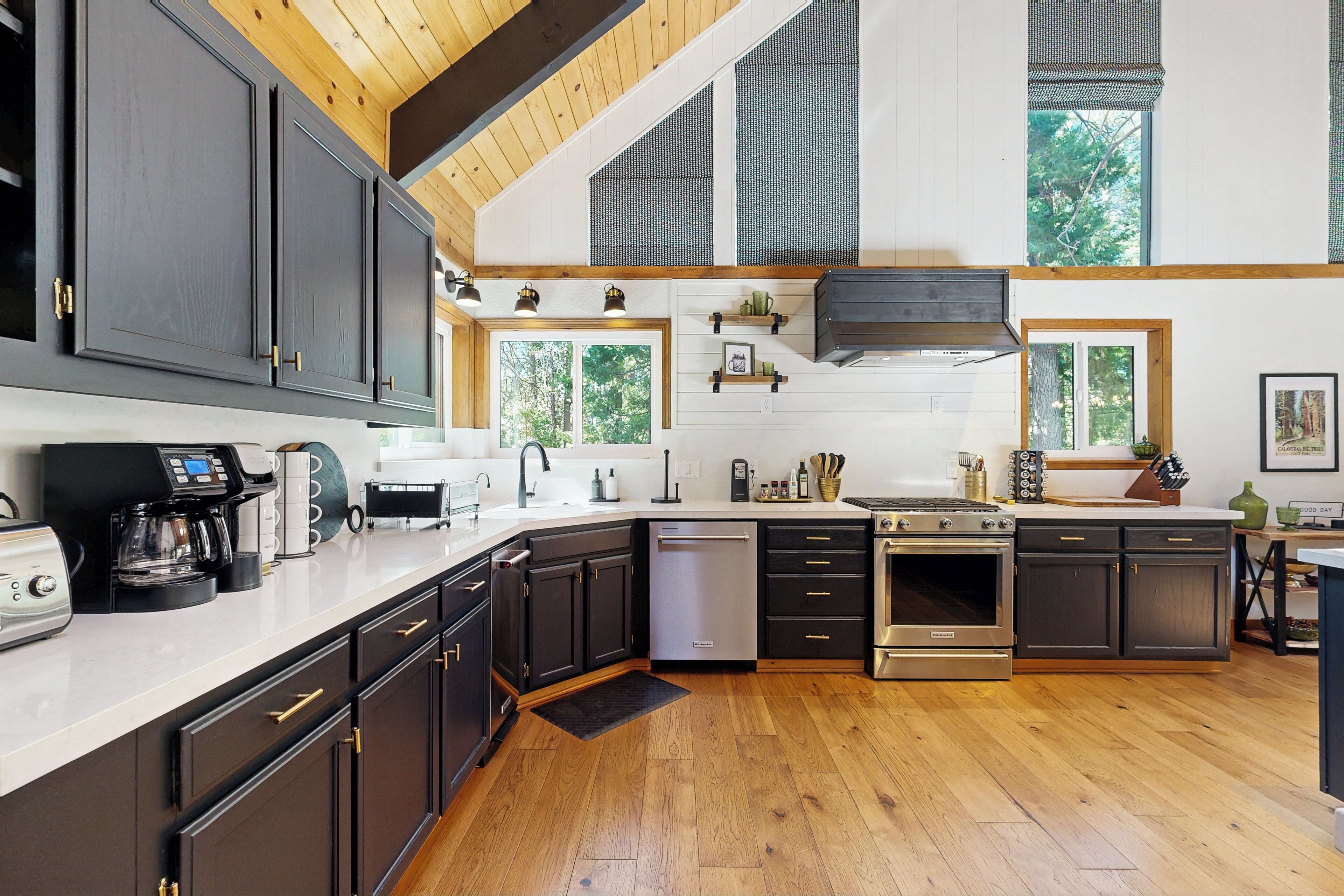 Une cuisine moderne avec des meubles de couleur sombre, des appareils électroménagers en acier inoxydable et un plancher en bois.