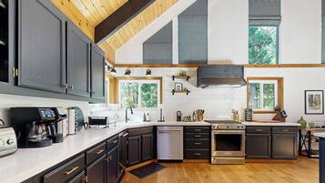 Une cuisine moderne avec des meubles de couleur sombre, des appareils électroménagers en acier inoxydable et un plancher en bois.