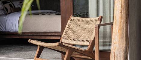 A wooden lounge chair by a poolside, with a concrete floor and a door in the background.