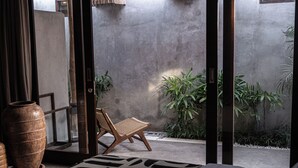 A modern room with a large bed, a wicker chair, and a concrete wall. - Kano Twin (Canggu)