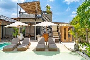 A poolside area with lounge chairs and umbrellas, a staircase, and a wooden structure with a thatched roof. - Kano Twin (Canggu)