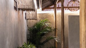 A narrow pathway with stone slabs and gravel, flanked by lush green plants and a wooden pergola structure. - Kano Twin (Canggu)