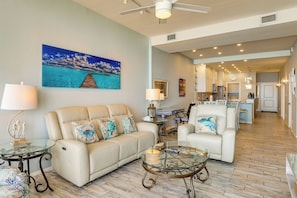 A spacious living area with a sofa, armchair, glass coffee table, and a painting of a tropical scene. - 2BR Penthouse Beach Perch: Suntide III - Unit 1207 (South Padre Island)
