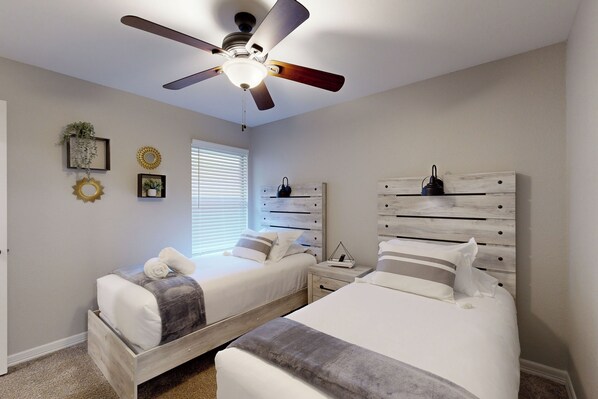 Quarto com duas camas, ventilador de teto e janela com persianas.