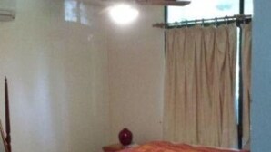 Un dormitorio con una cama individual, ventilador de techo, ventana con cortinas y una mesita con un florero.