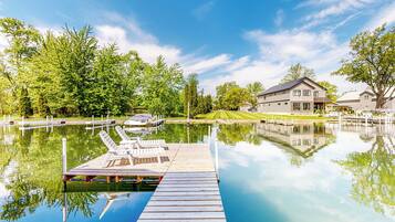 Une jetée en bois s’étendant sur un lac paisible, avec une maison en arrière-plan.