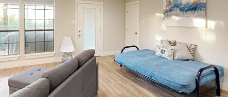 Ein modernes Wohnzimmer mit einem grauen Ecksofa, einem blauen Liegebett und einer weißen Stehlampe.