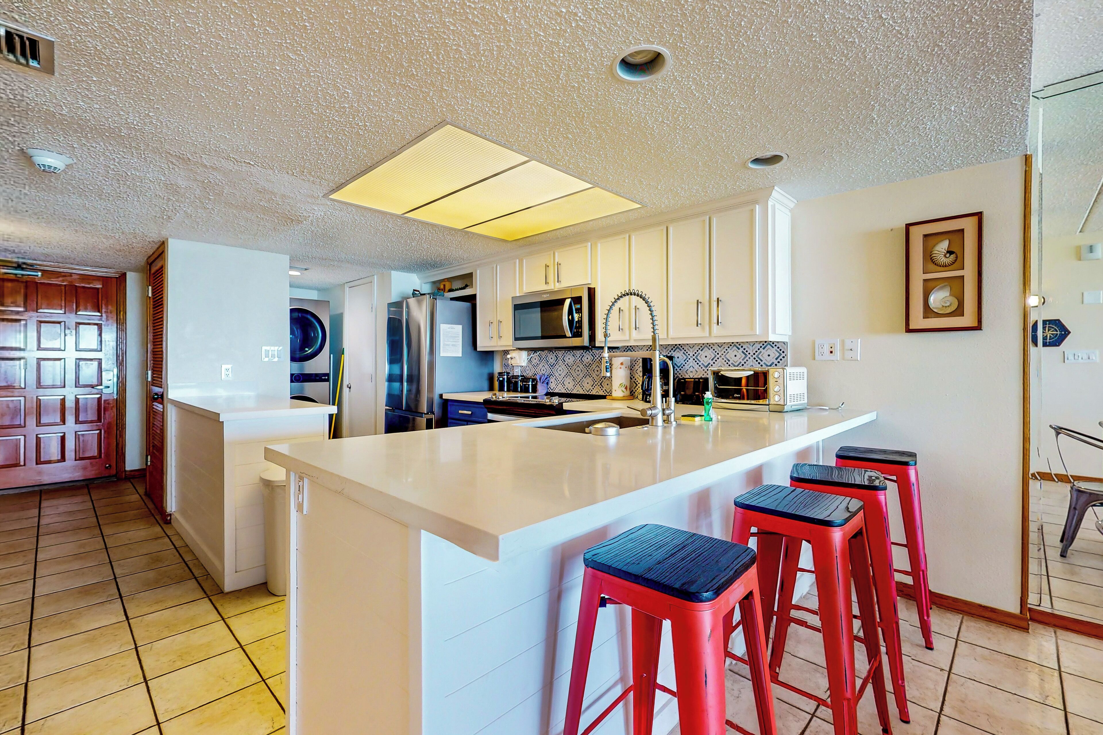 A modern kitchen with a central island, bar stools, and a microwave.